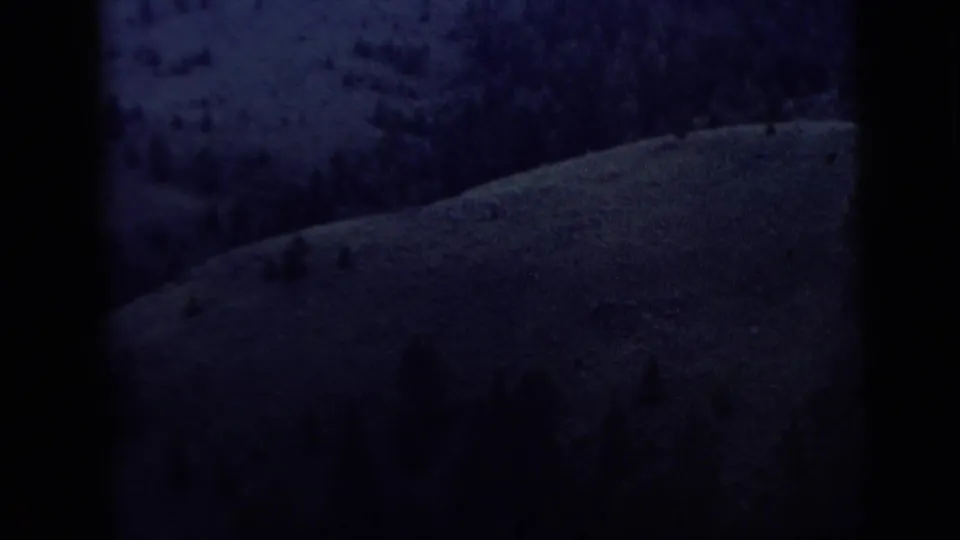 Underexposed 8mm frame showing a sloped hillside with sparse trees or brush.