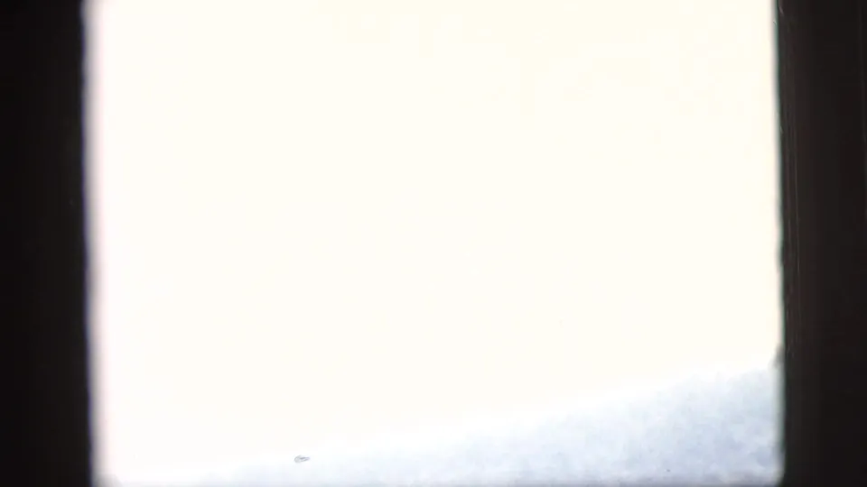 Overexposed closing frame with pale sky, a faint hillside edge, and dark film borders.