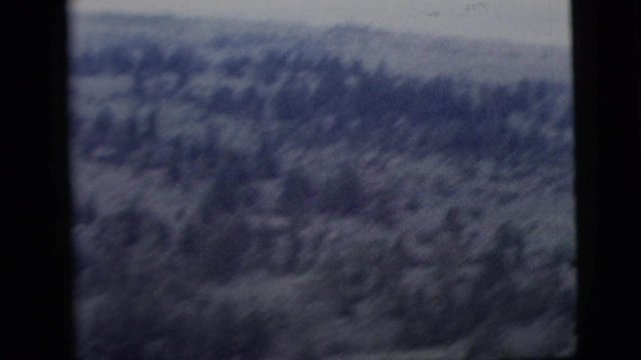 1958 8mm home-movie frame with a hazy, soft-focus view of wooded hills or mountains, partly obscured by film frame borders.