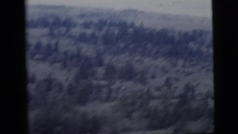 1958 8mm home-movie frame with a hazy, soft-focus view of wooded hills or mountains, partly obscured by film frame borders.