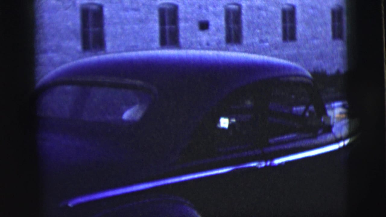 Dark rounded sedan seen from the side near a brick building at night.