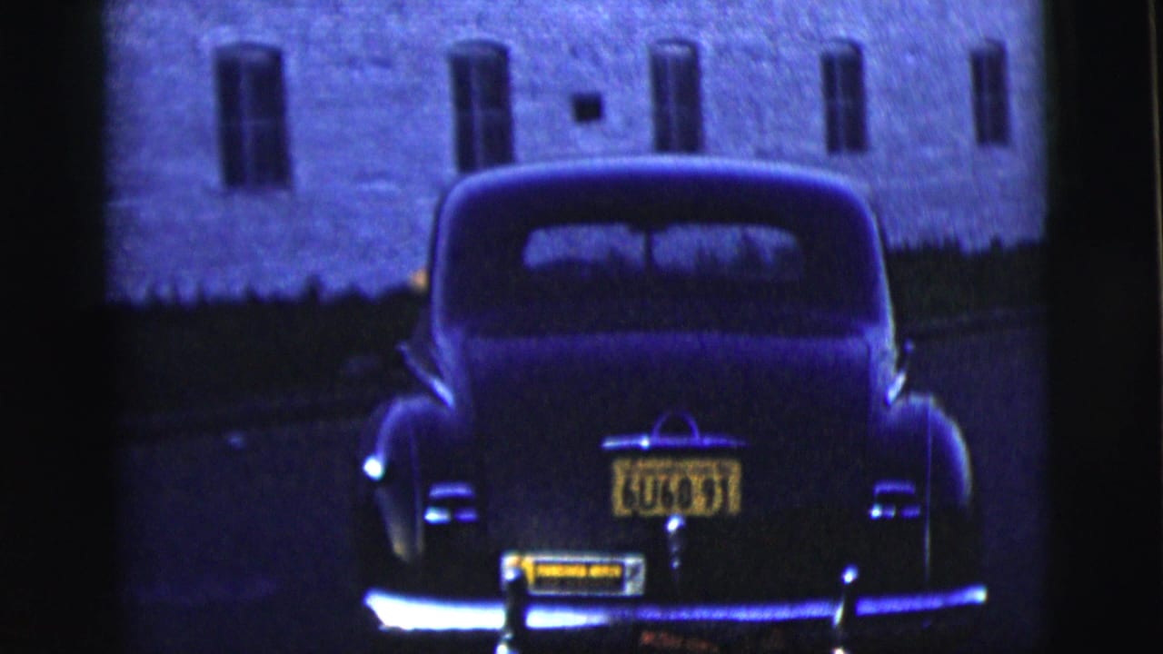 Rear view of a dark sedan with yellow plates in front of a brick building.