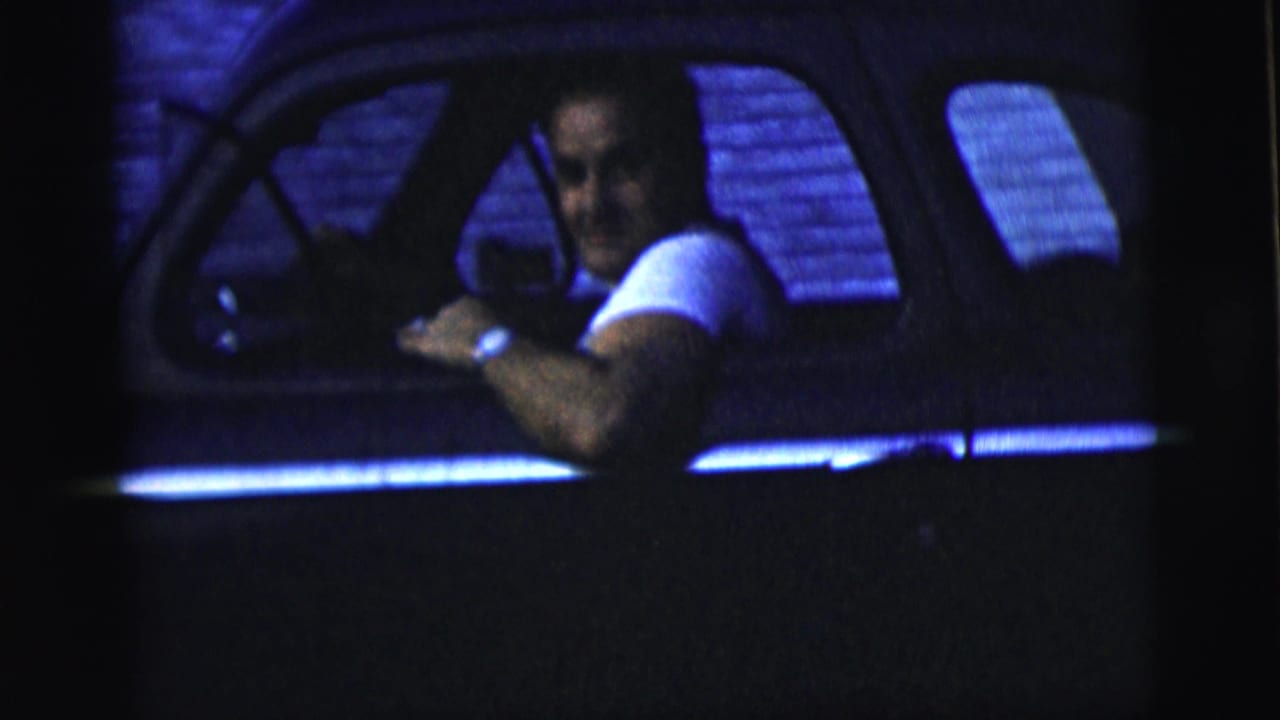 Man in a white T-shirt looks from a car window at night.