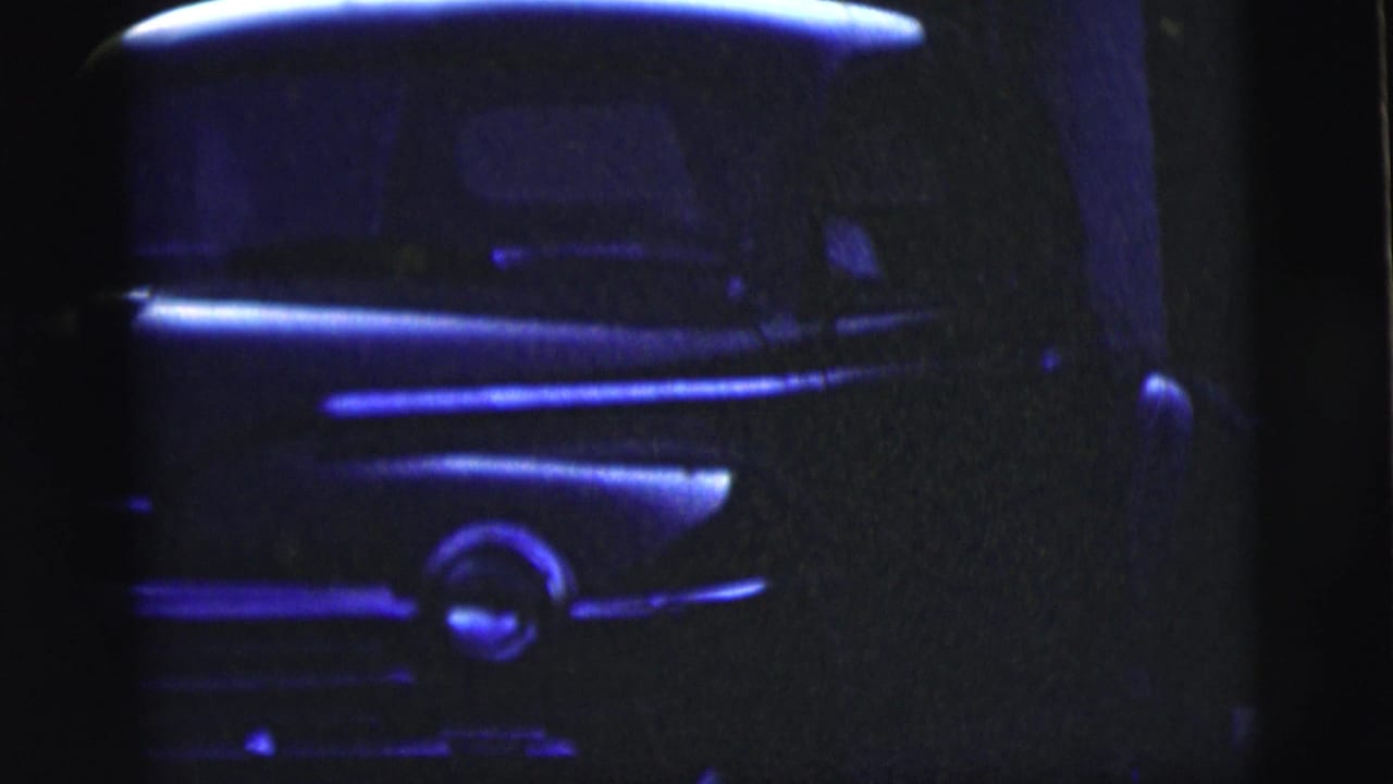 Blue-tinted close view of a classic car front end and headlight area.