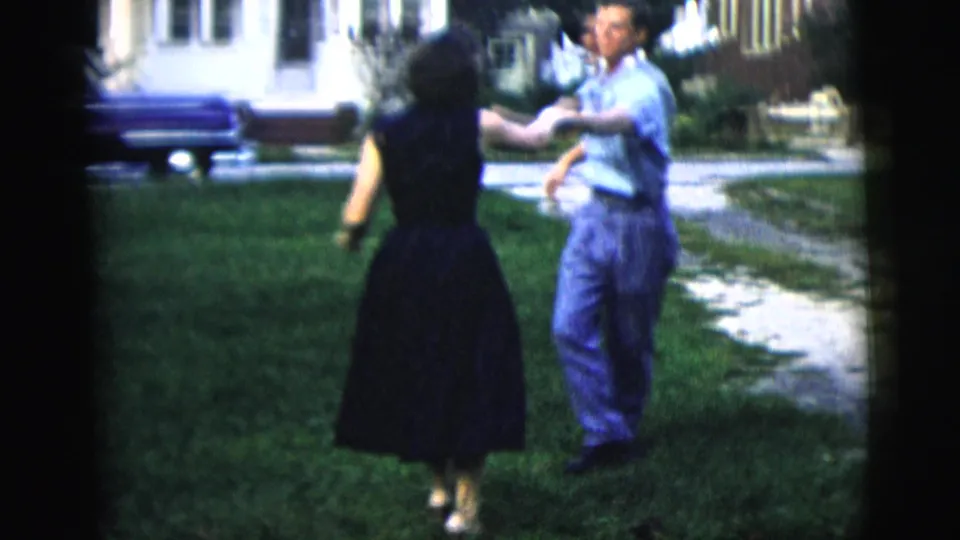 1958 New York City home-movie frame showing a man in a light shirt dancing with a woman in a dark dress on a residential lawn.