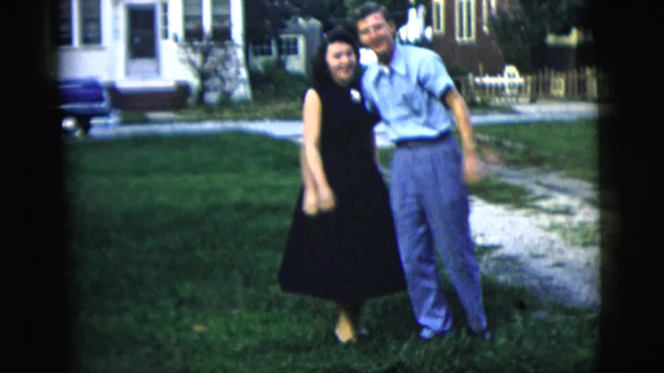 The couple faces the camera on a residential lawn, with the man leaning toward the woman in a casual 1958 home-movie pose.