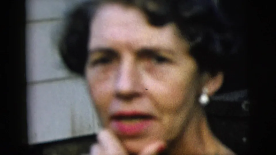 Close-up of a woman with styled dark hair, red lipstick, and pearl earring in soft 8mm focus.
