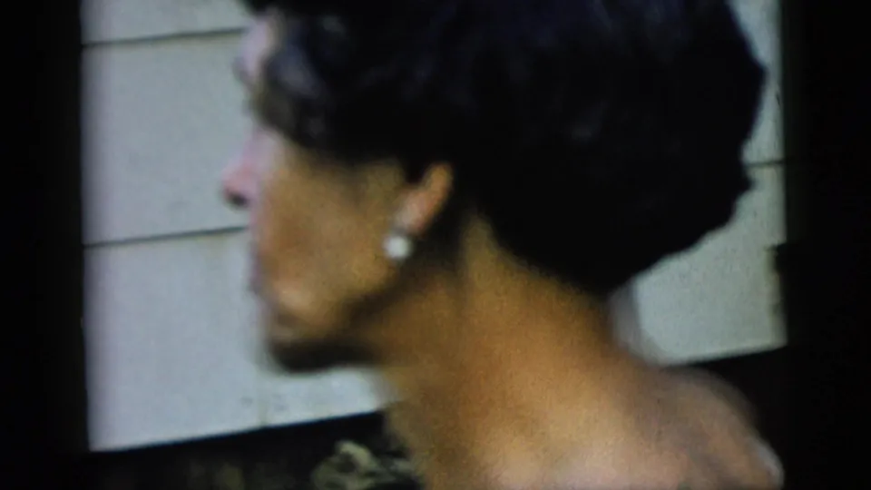 Profile view of the woman near exterior siding, showing dark curled hair and a pearl earring in soft 8mm color.