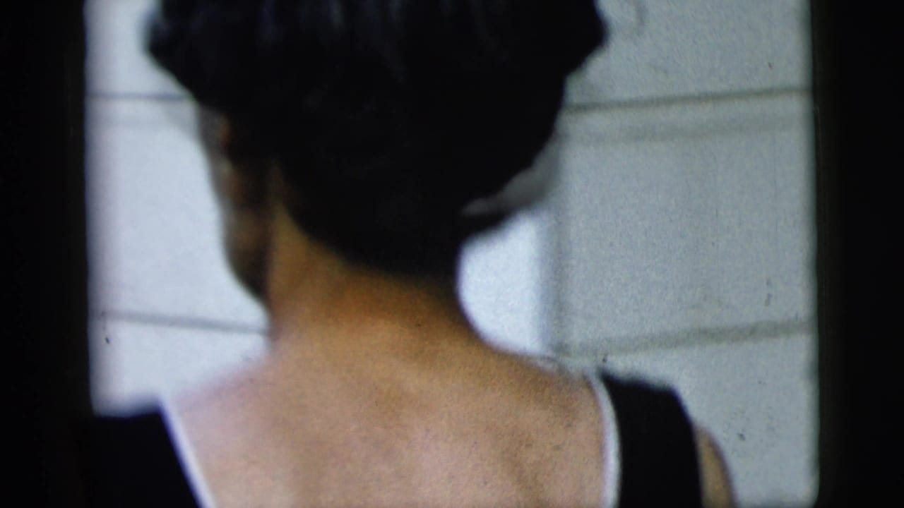 Back of a woman in a dark sleeveless dress near white house siding.