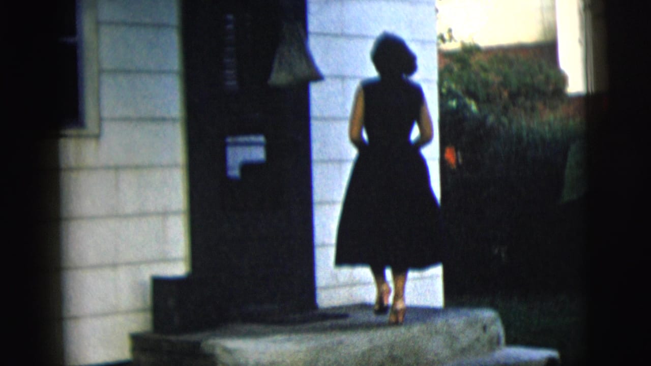 Woman in a black dress stands on front steps facing a dark doorway.