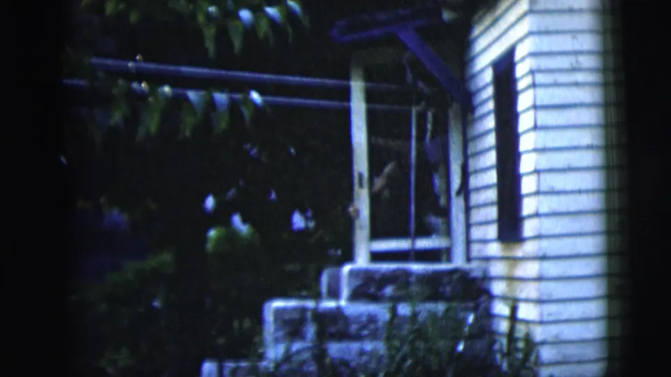 A nighttime 1958 New York City exterior shows a white-sided house, screen door, stone steps, and surrounding foliage.