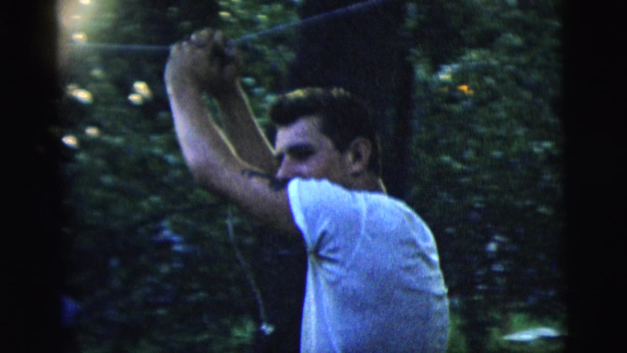 In 1958 New York City home-movie footage, a young man in a white T-shirt lifts a long pole near backyard trees.
