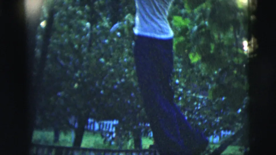 A man in a white T-shirt and dark pants hangs from a tree branch beside a large trunk in the 1958 New York City clip.