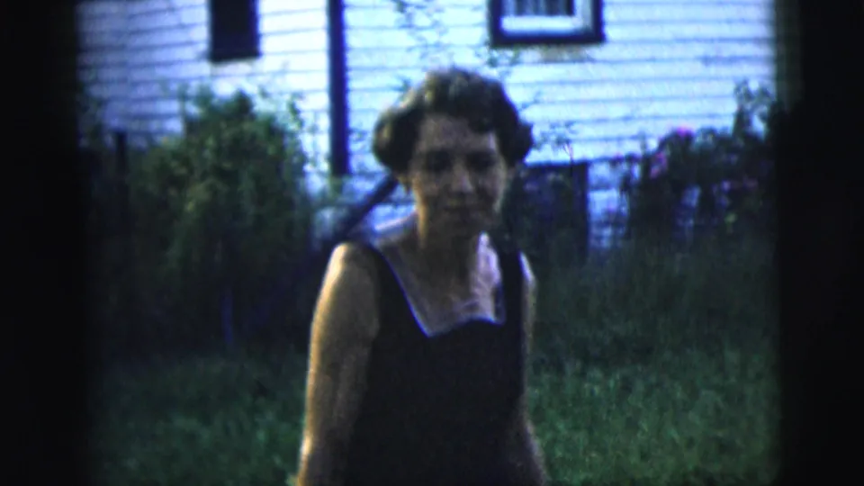 1958 New York City home-movie frame with a closer view of the woman approaching the camera in a residential backyard.