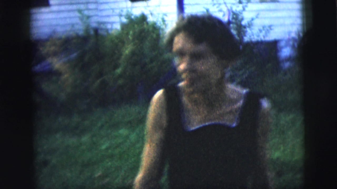 Adult woman in a dark dress with a light collar appears in a New York City backyard in 1958 home-movie footage.