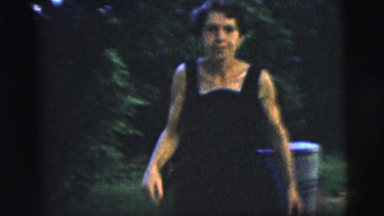 Adult woman walks toward the camera in a leafy backyard, wearing a dark dress and heels in 1958 New York City footage.
