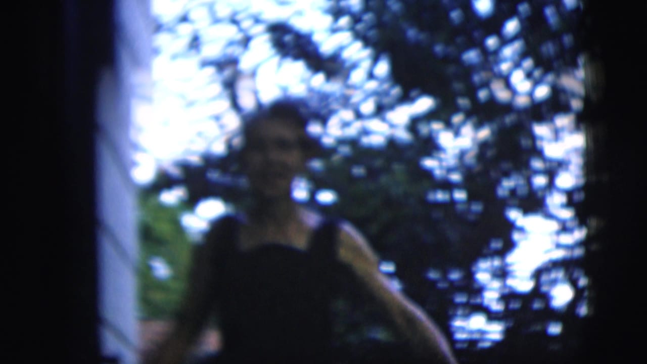 Woman in a dark dress stands under trees near a residential exterior.