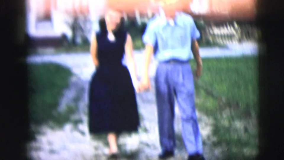 A couple walks together along a residential yard path, with the upper frame partly obscured by blur or film exposure.