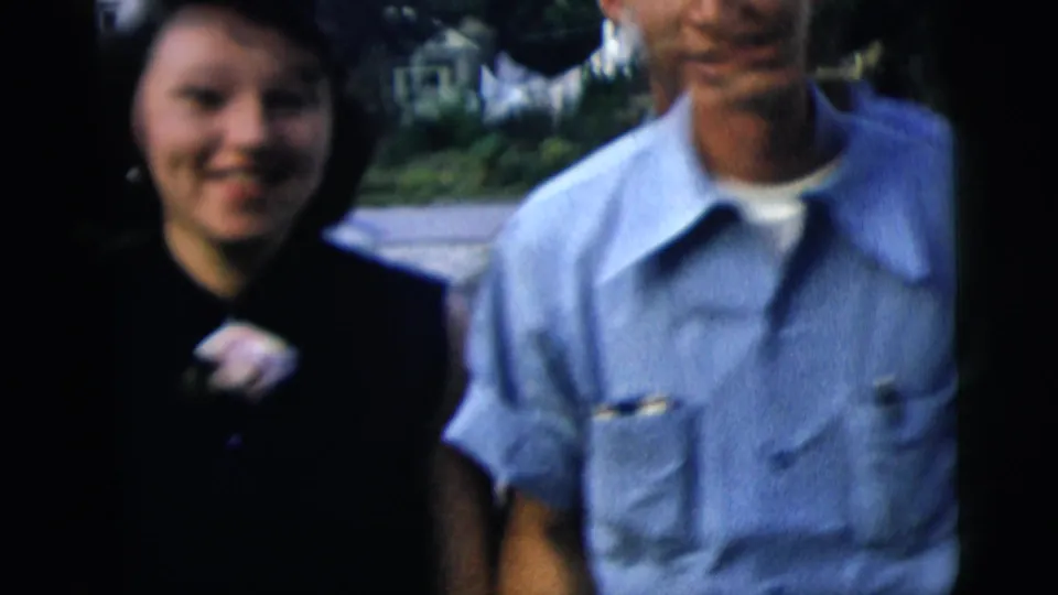 The couple moves close to the camera, with the woman's face, brooch, and the man's light shirt visible in soft 8mm focus.