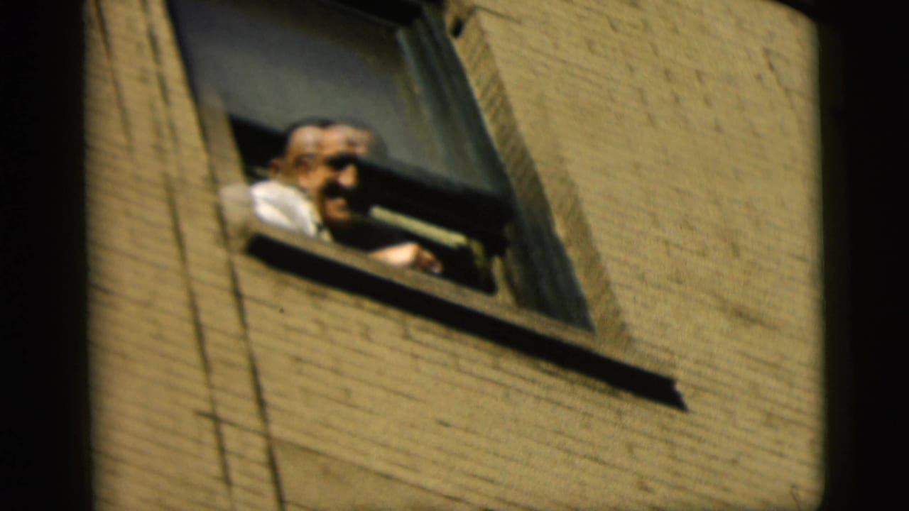 In 1958 New York City home-movie footage, a smiling man leans from an open window above a brick wall.