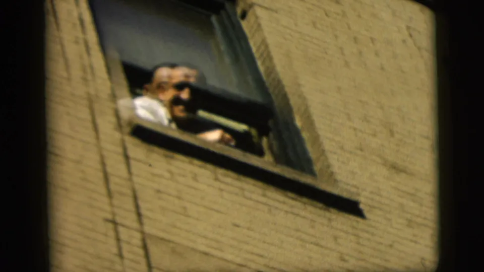 In 1958 New York City home-movie footage, a smiling man leans from an open window above a brick wall.