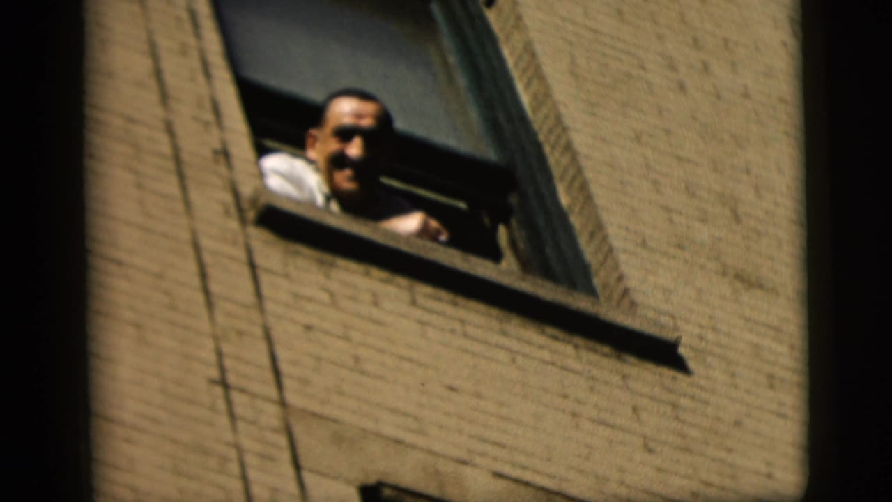 Smiling man rests at an open window in a brick building.