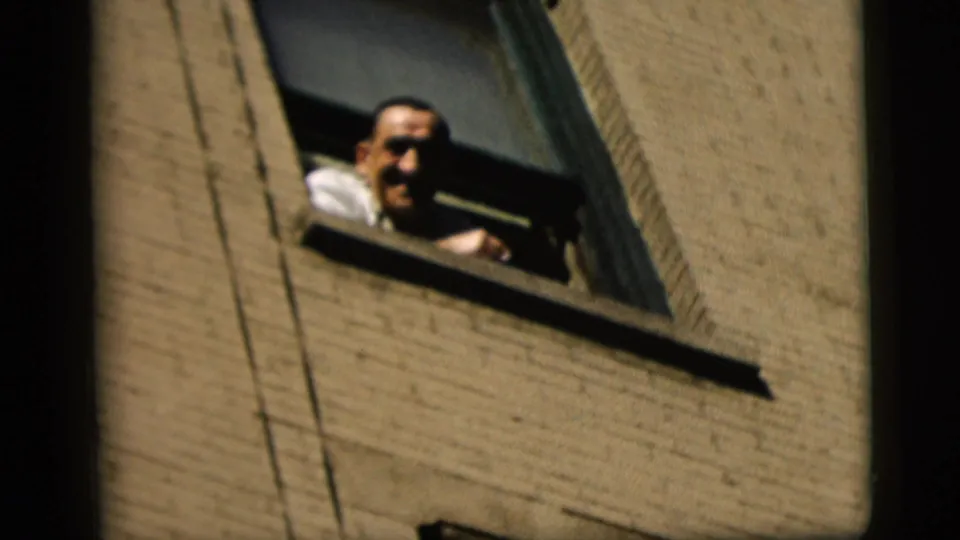 The man leans farther from the open window, facing downward in a candid 1958 New York City home-movie moment.