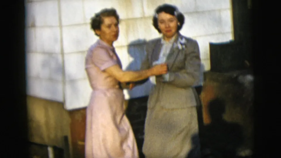A friend in a pink dress embraces or adjusts the suited woman with corsage during a brief celebratory pose in New York City.