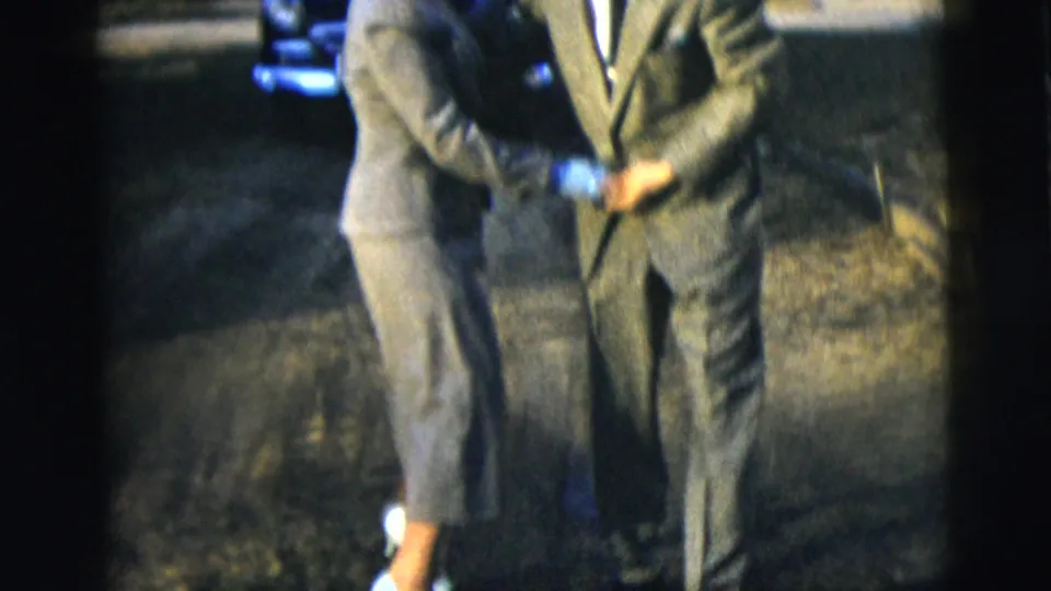 The dancing couple is seen in a tighter, partly cropped 1958 home-movie frame, showing suits, hands, and outdoor lawn detail.