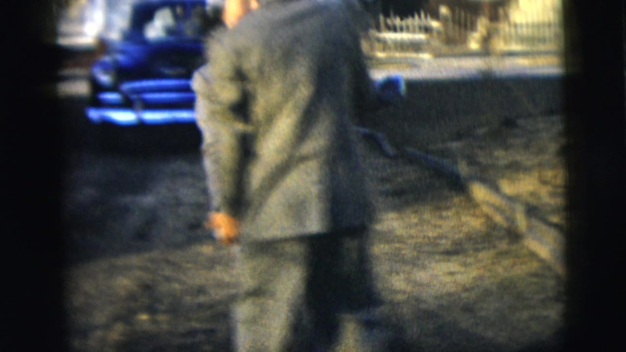 Suited man seen from behind walking or turning on a sunlit driveway.