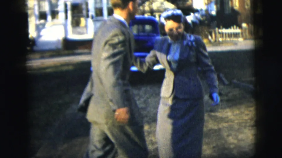 The couple dances in formal mid-century clothing, with the woman wearing gloves and a hat near a blue car in the background.
