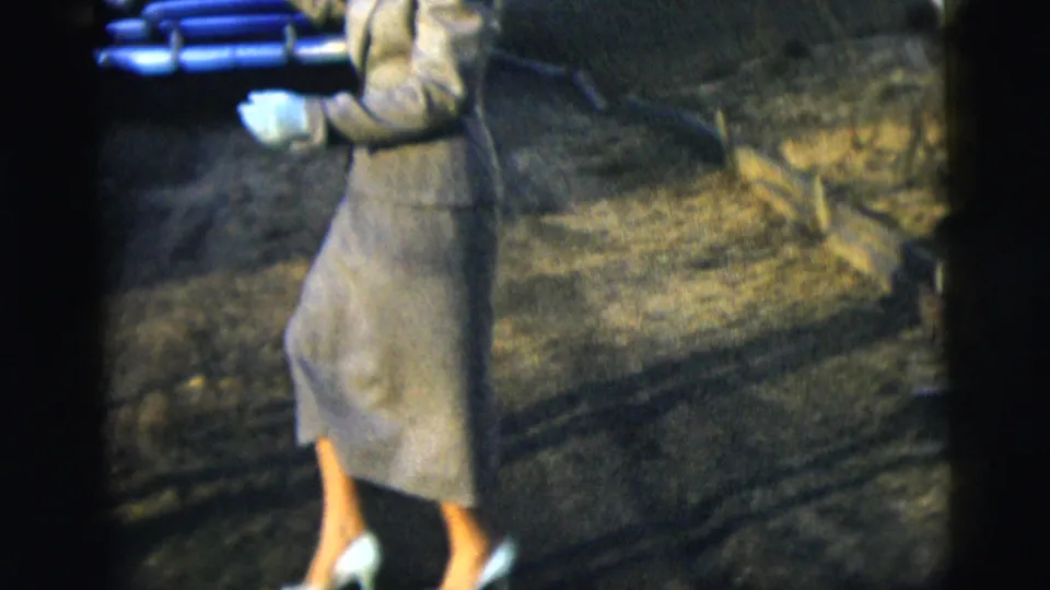 The frame catches the woman's skirt suit, white gloves, and heels as she steps during the driveway dance.