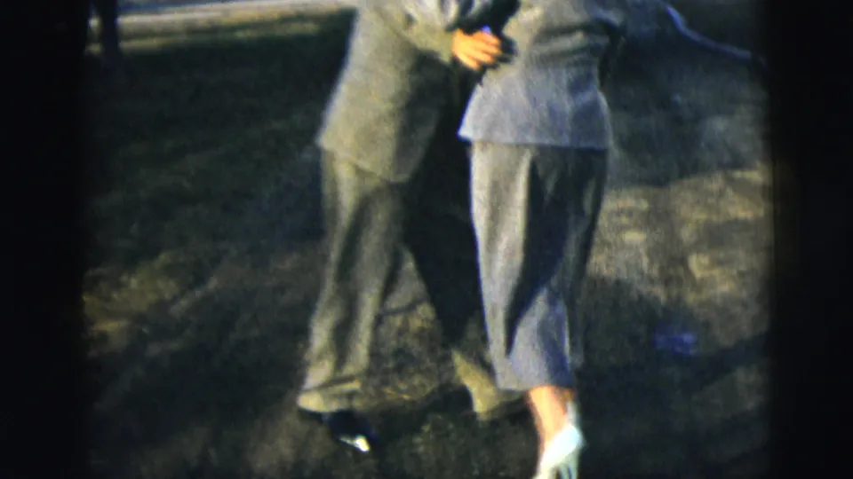 In a 1958 New York City home-movie frame, a formally dressed couple dances closely on a residential street, partly cropped by the camera.