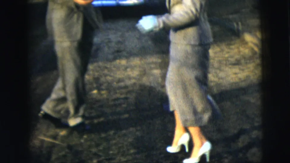The formally dressed couple continues their close dance on a New York City residential street, with the woman in white heels and the man in a dark suit.