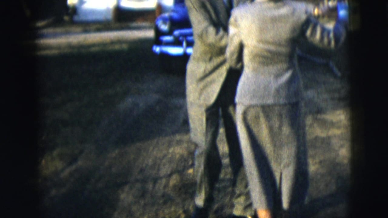 A man and woman in gray formal attire dance together on a lawn in 1958 New York home-movie footage.