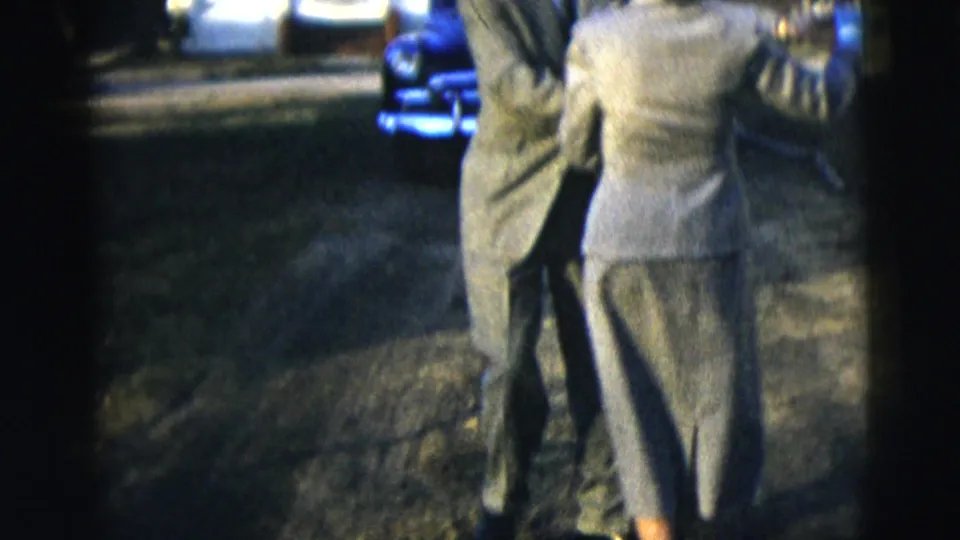 A man and woman in gray formal attire dance together on a lawn in 1958 New York home-movie footage.