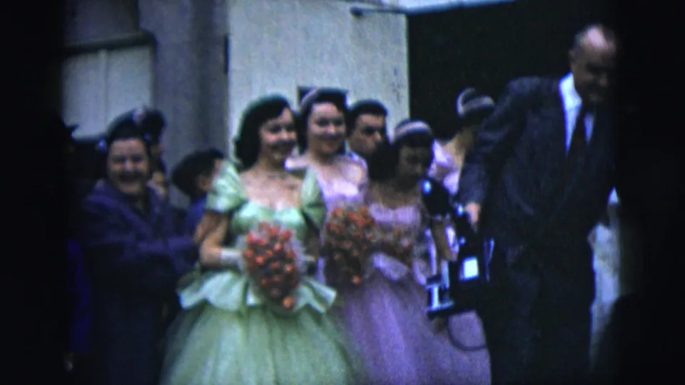 A bridal party in 1958 New York City walks past the camera, with bridesmaids in pastel dresses carrying bouquets and guests clustered nearby.