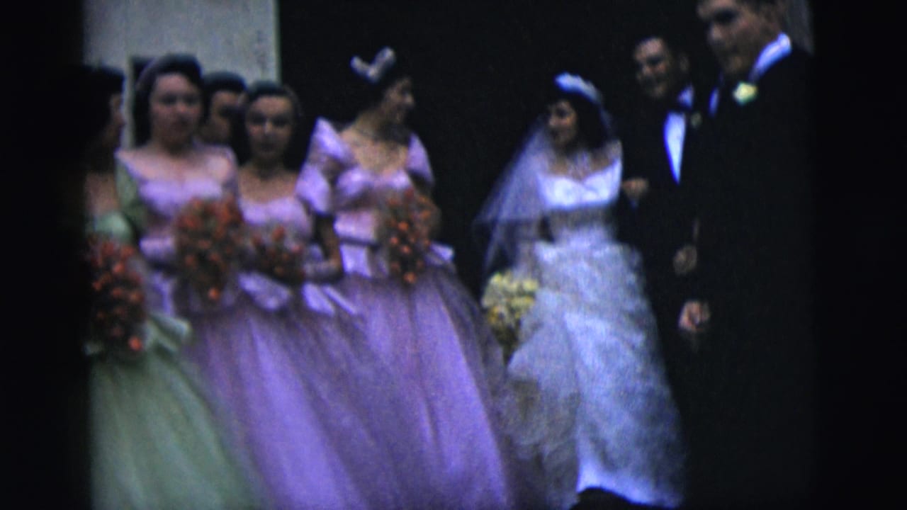 Bride and groom walk with bridesmaids carrying bouquets in a dim indoor setting.