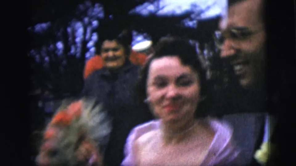 A close handheld outdoor view shows the bride smiling beside the groom, with guests gathered around them in 1958 New York City.