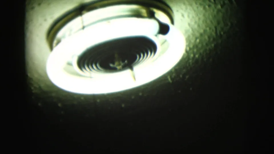 Close-up of a glowing ceiling light fixture in grainy 8mm footage, likely an interior domestic detail from the same 1958 reel.