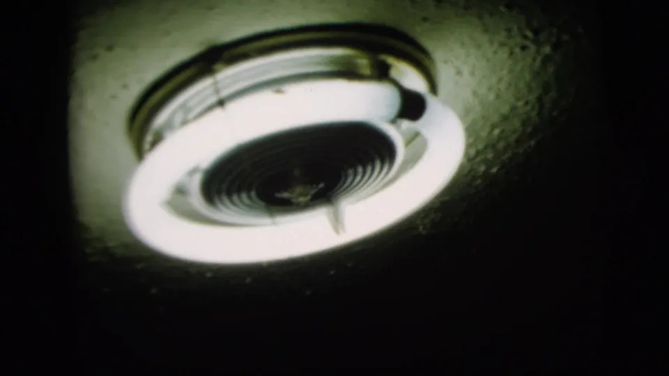Later frame of the same interior ceiling light fixture, with soft focus, visible grain, and high contrast from the bright lamp.