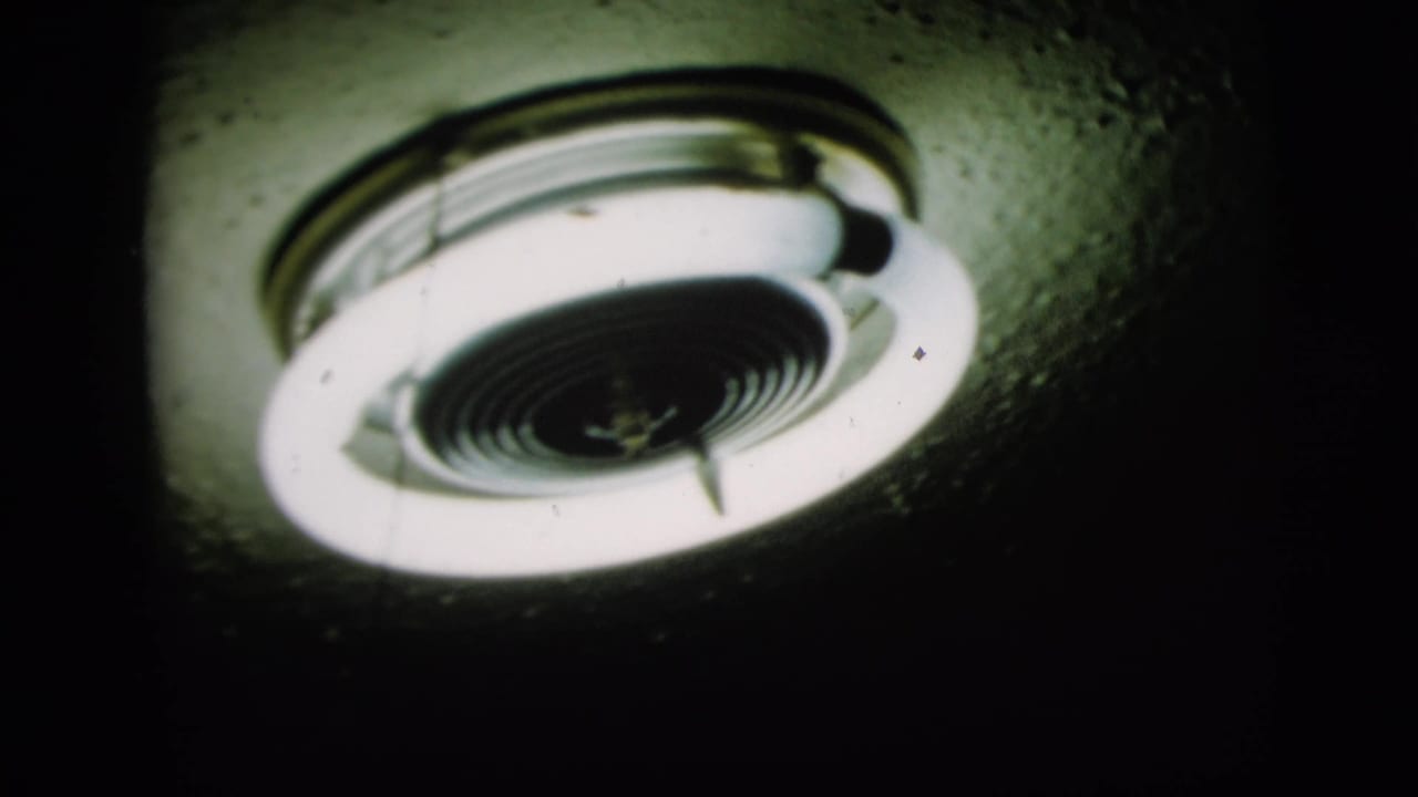 1958 New York 8mm frame showing two illuminated round fluorescent ceiling fixtures from below in a dark interior.