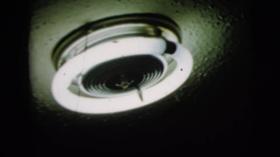 1958 New York 8mm frame showing two illuminated round fluorescent ceiling fixtures from below in a dark interior.