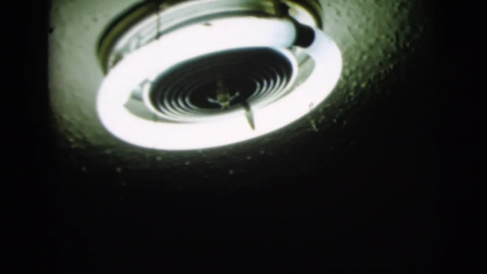 Close 8mm view of illuminated circular ceiling fixtures, with bright rings and soft focus in a dark 1958 New York interior.