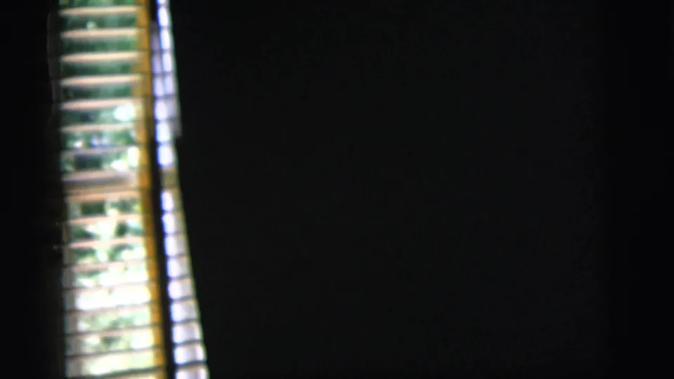A dark 1958 home-movie frame shows venetian blinds, bright daylight, and foliage glimpsed through the window.