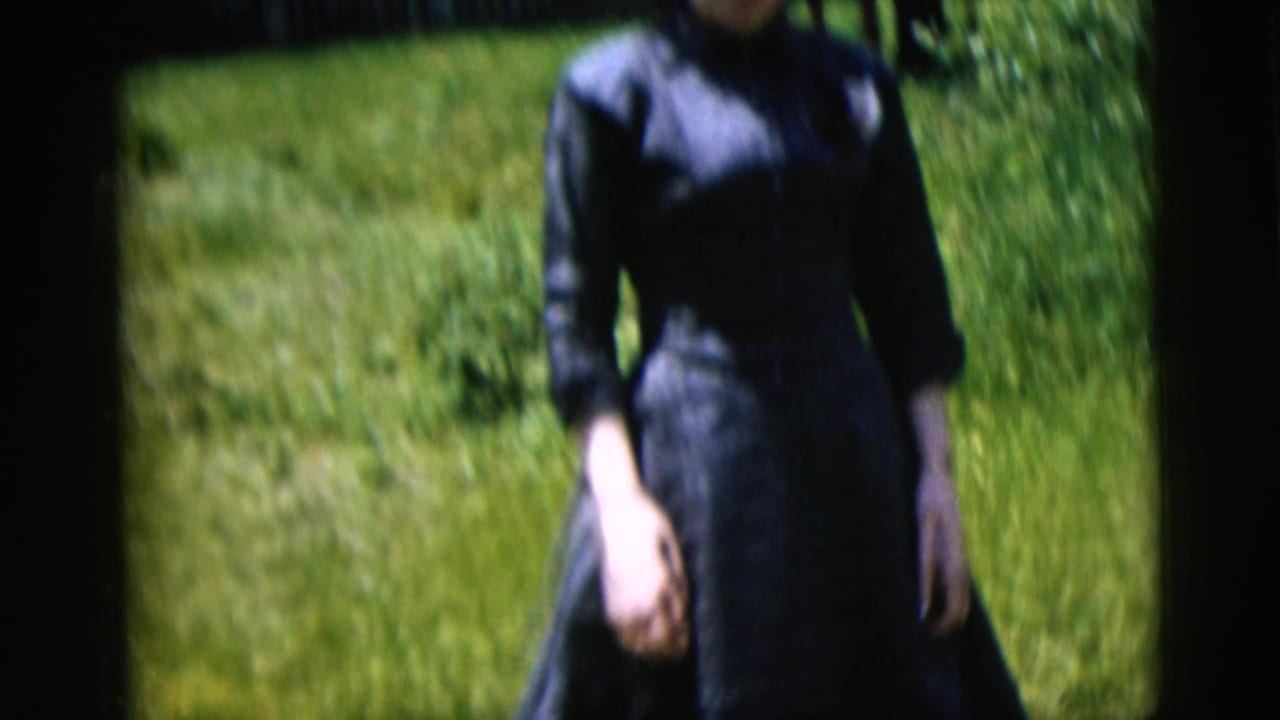 1958 New York City home-movie frame of a woman in a dark blue dress walking toward the camera in a grassy yard.