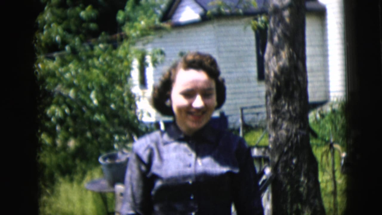 Woman smiling beside a tree with a white house and yard greenery in the background.