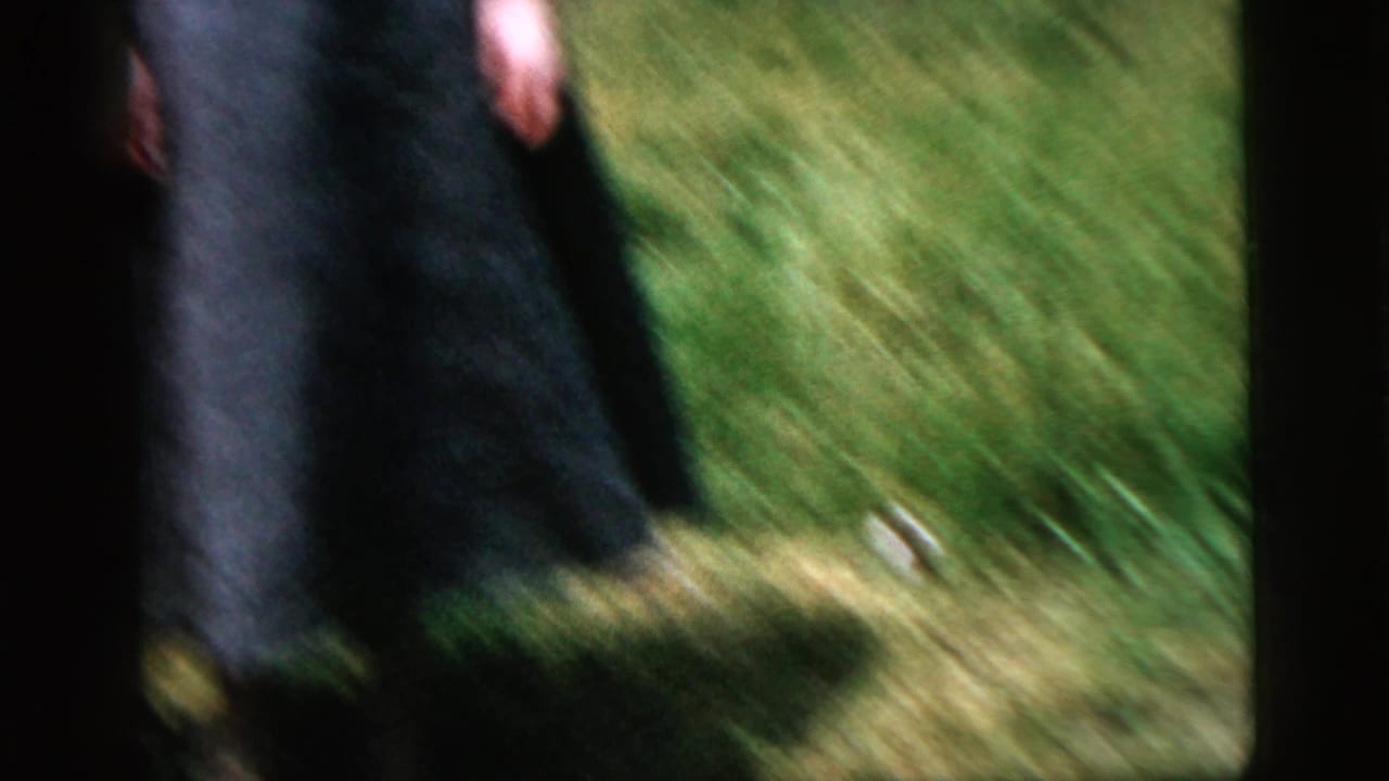 Blurred figure crossing sunlit grass beside a dark frame edge.