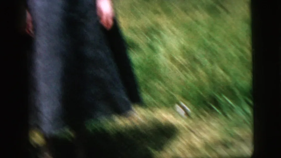 A blurred person moves through bright grass in 1958 8mm home-movie footage, with heavy motion blur and dark frame borders.
