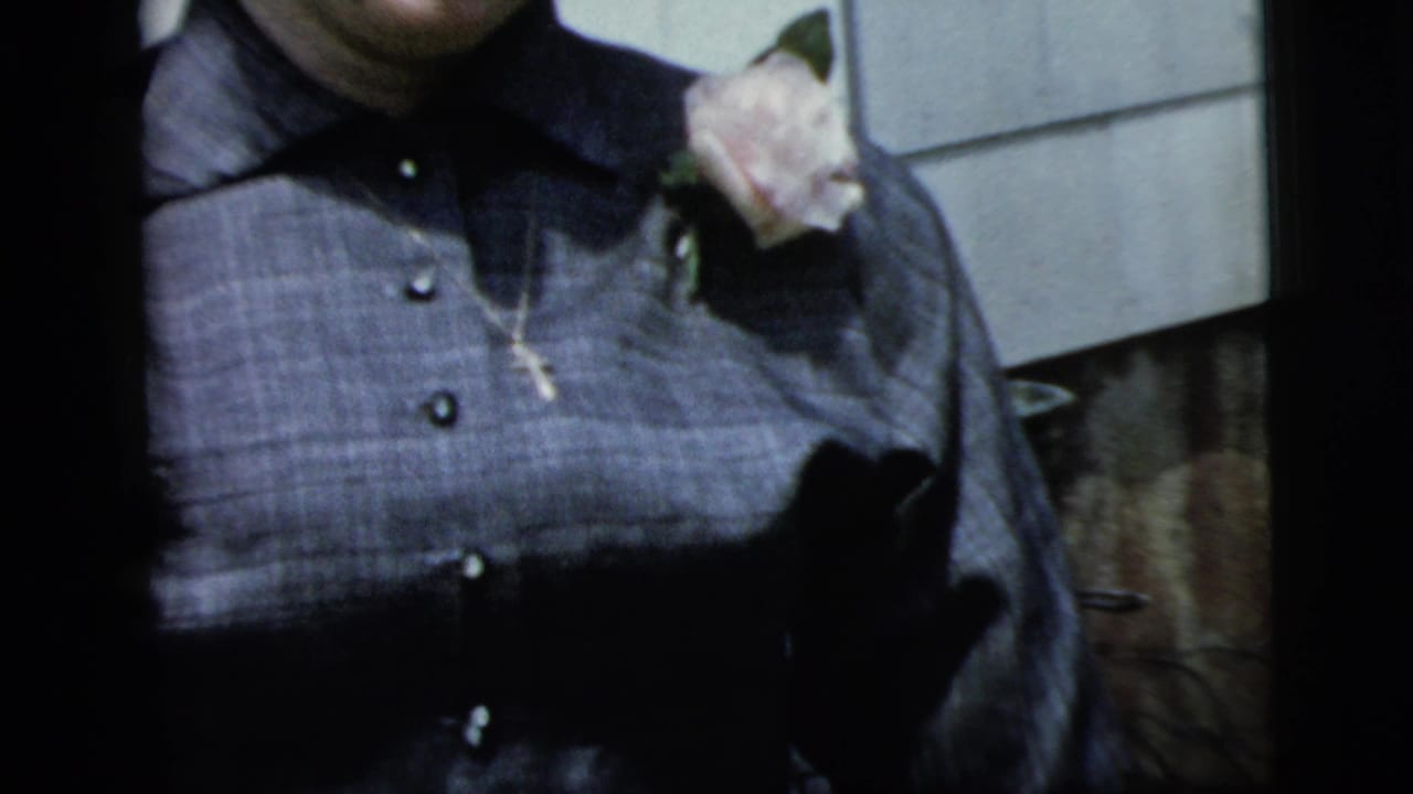 Cropped view of a woman in a dark blouse with a pale rose pinned near her shoulder.